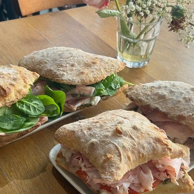 Des panini à la ciabatta, jambon et pousses d'épinards, sur une table en bois